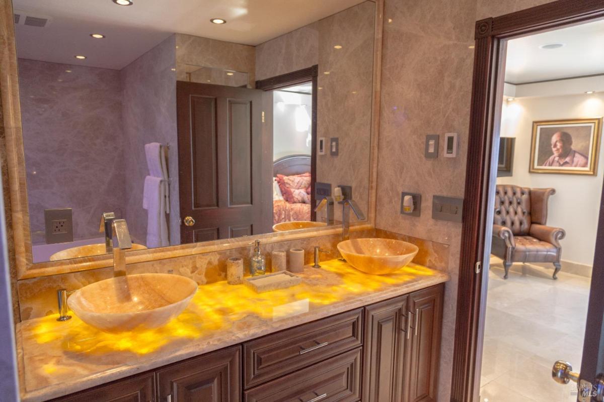 A bathroom with dual stone sinks on a wooden vanity, illuminated from below.