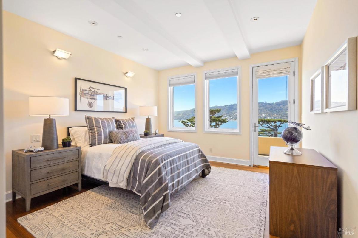 Bedroom with a striped bedspread, two nightstands, and a door leading to a balcony overlooking the ocean.