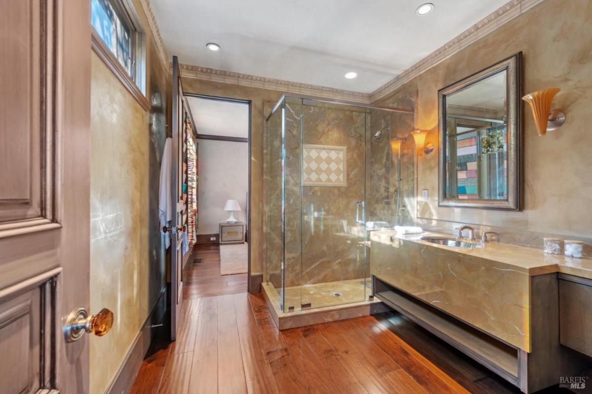 Bathroom with a glass shower and a sleek double vanity, featuring warm wooden flooring and elegant lighting.