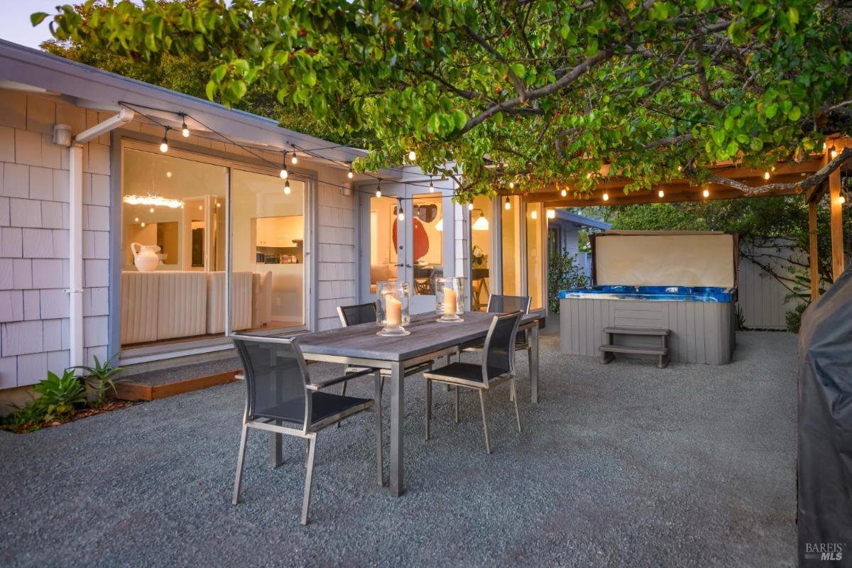 Outdoor dining area with a hot tub under a pergola and string lights.