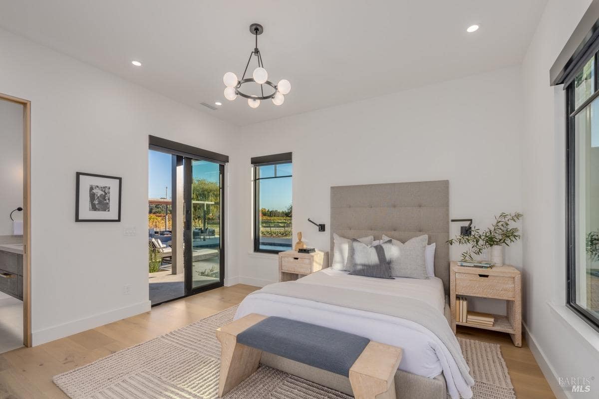 A bedroom with a large bed, wood nightstands, sliding glass doors, and windows providing outdoor views.