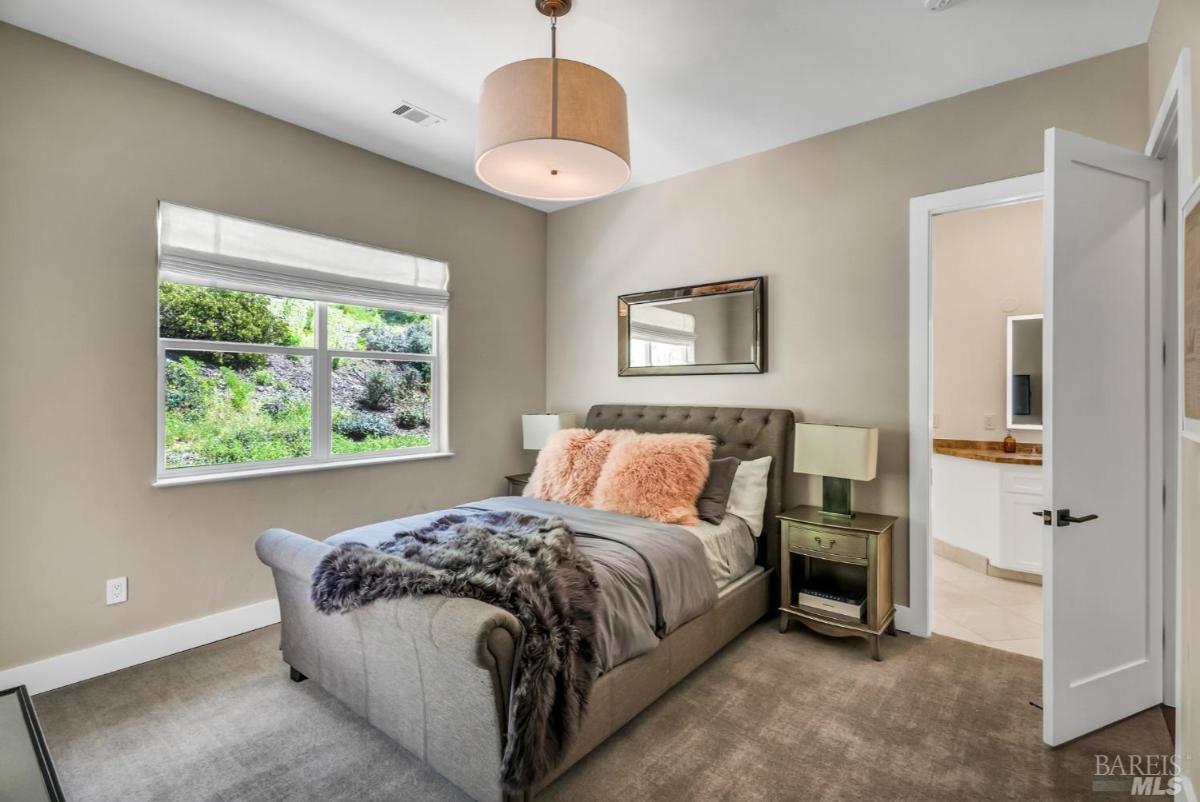 A bedroom featuring a bed with pillows, a window, and a doorway leading to a bathroom. 