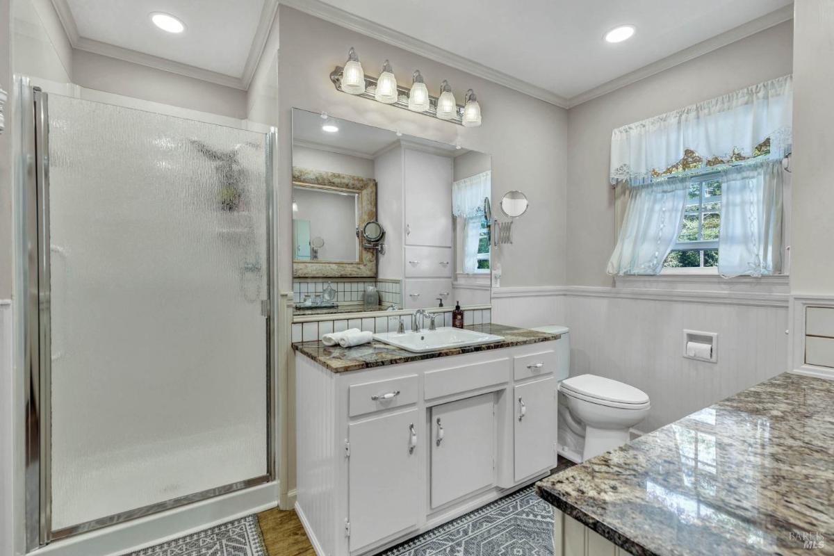 A bathroom with a glass-enclosed shower, double vanity, and granite countertops.