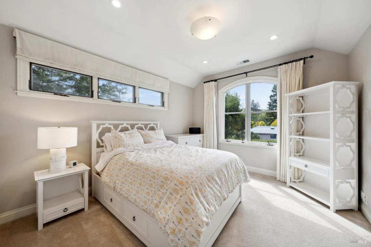 A bedroom with built-in shelving, a bed with storage drawers, and an arched window.