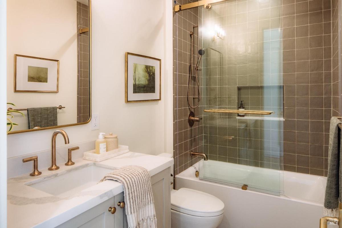 A bathroom with a shower-tub combo, dual sinks, and framed artwork on the walls.