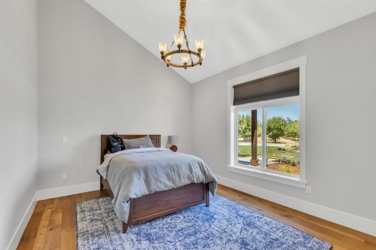 A bedroom contains a bed, a lamp, and a window overlooking a garden.