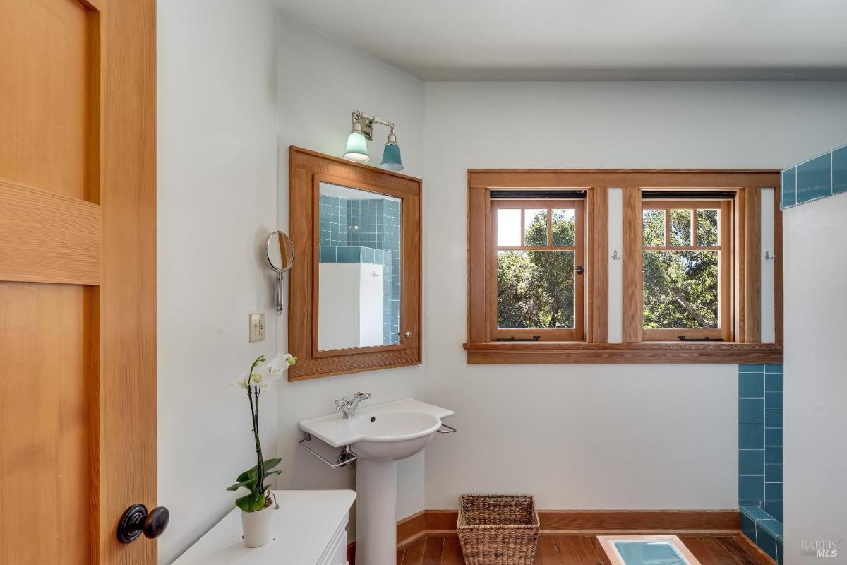 Bathroom with a sink, mirror, and windows above a tiled shower area.