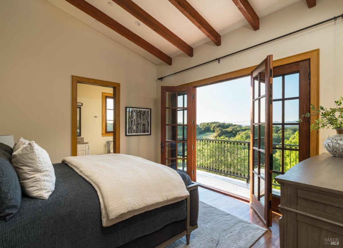 Bedroom with balcony overlooking green landscape.