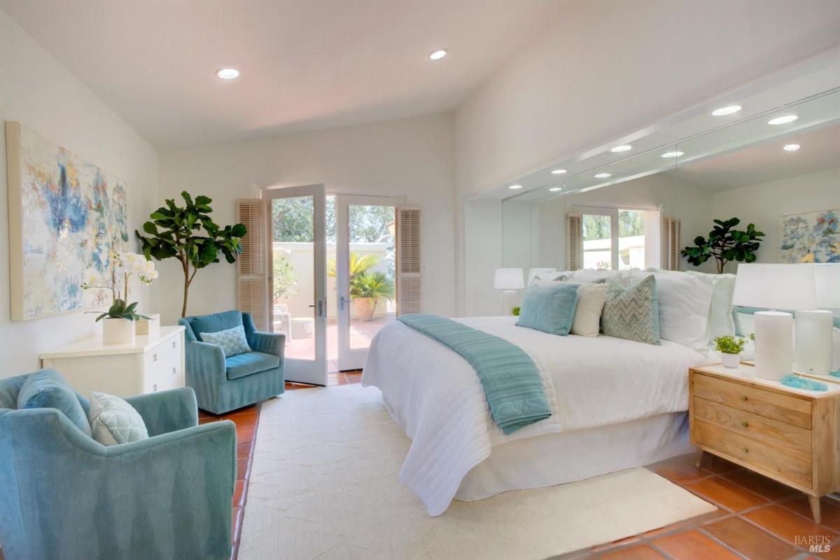 A bedroom with mirrored walls, chairs, and doors opening to a private outdoor area.