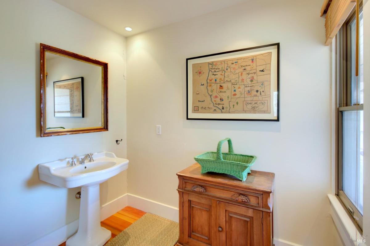 A powder room with a pedestal sink, a framed map on the wall, and a wooden cabinet.