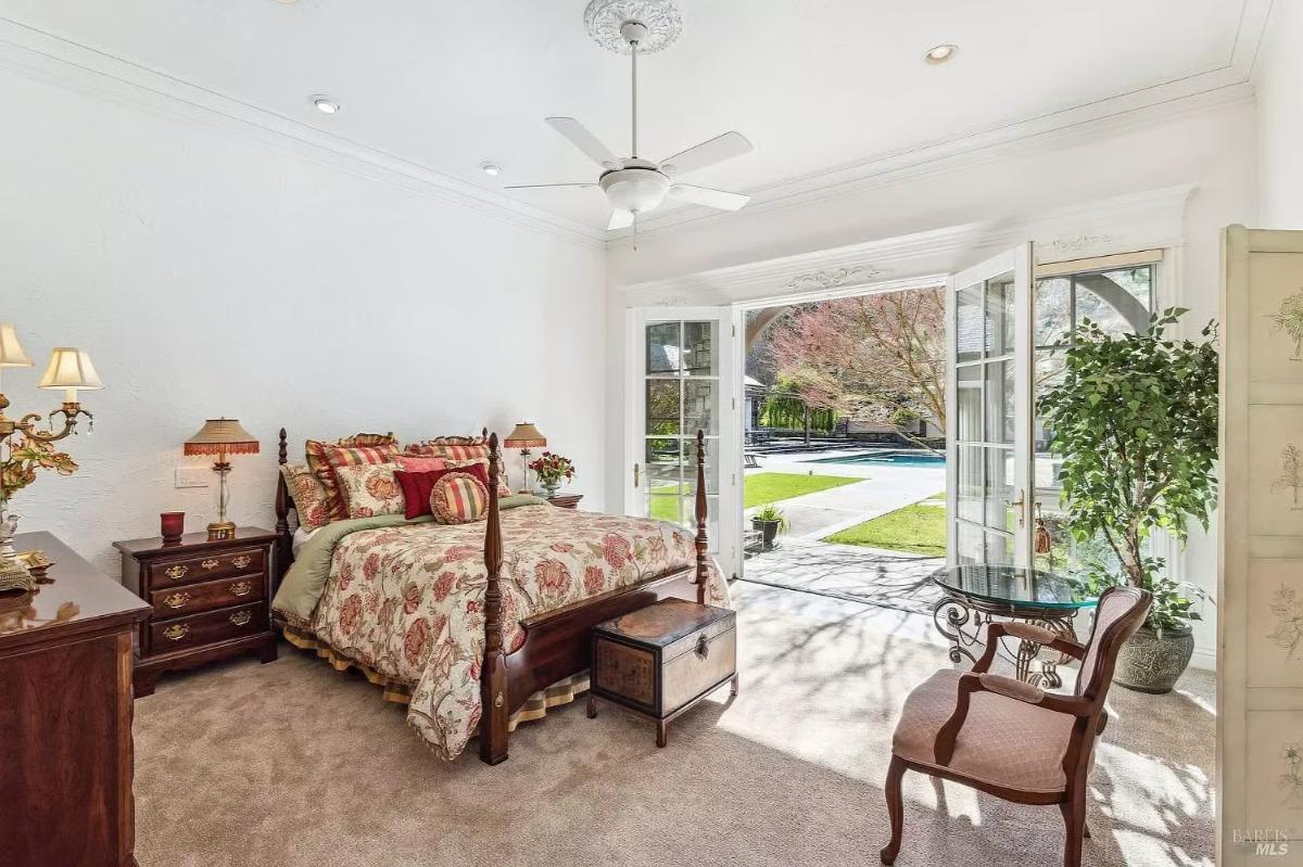 Bedroom with a wooden bed, patterned bedding, and French doors opening to a pool area.