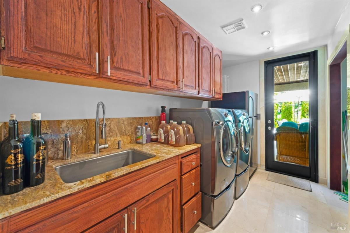 A laundry room featuring wooden cabinets above a countertop with a sink.