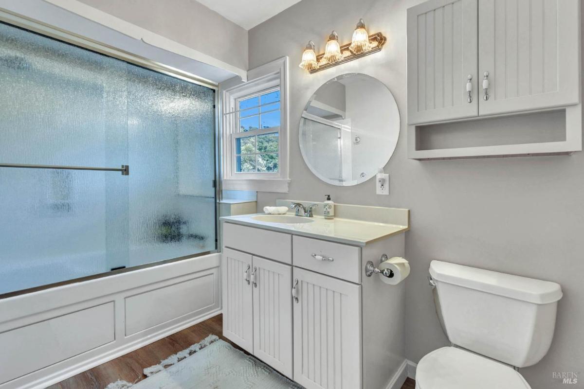 A bathroom with a bathtub, white vanity, and round mirror over the sink.