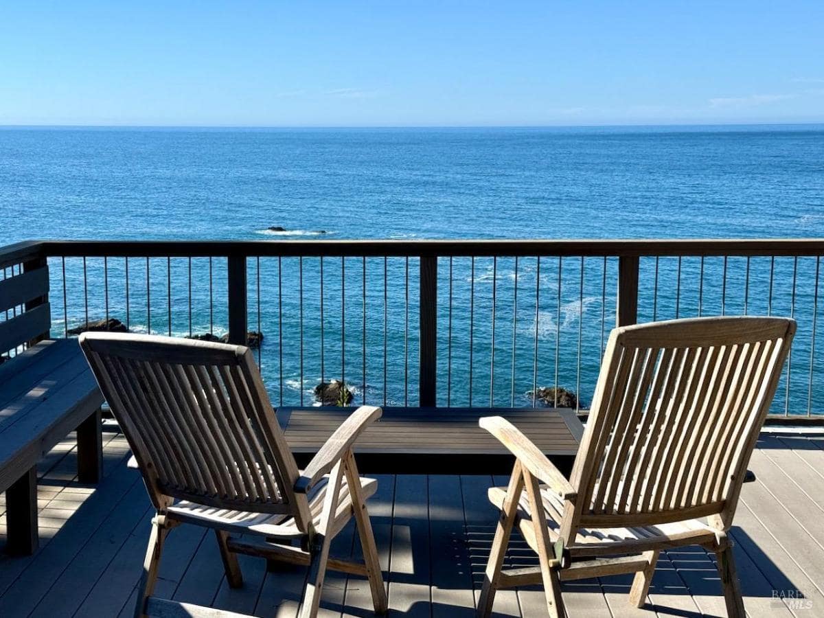 A deck with two wooden chairs overlooking the ocean.