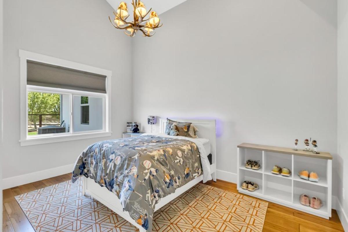 A bedroom features a bed with a patterned blanket, a shelf for shoes, and a window with a view of the outdoors.