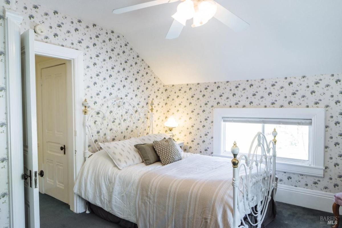 A bedroom with a white iron bed, floral wallpaper, and a window.