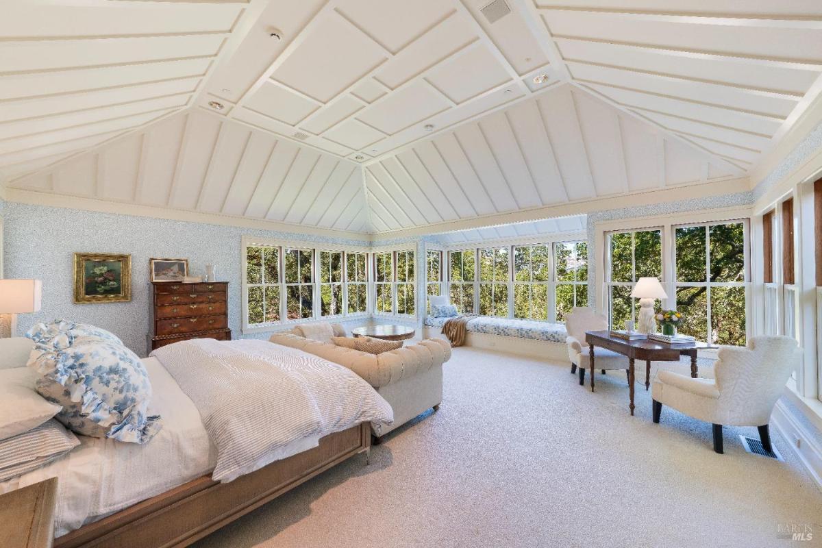 Large bedroom with a bed, seating area, and corner windows.