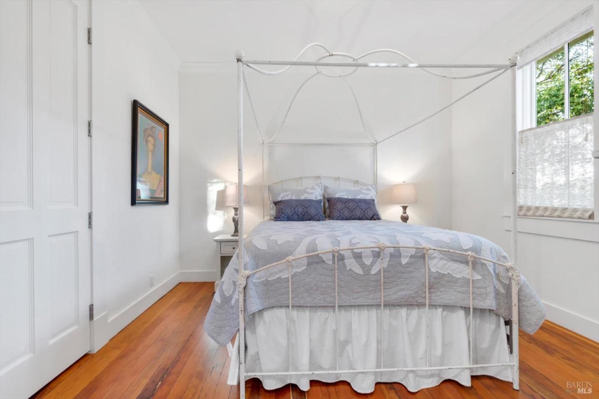 A bedroom bed with a wooden frame and two windows with blinds.