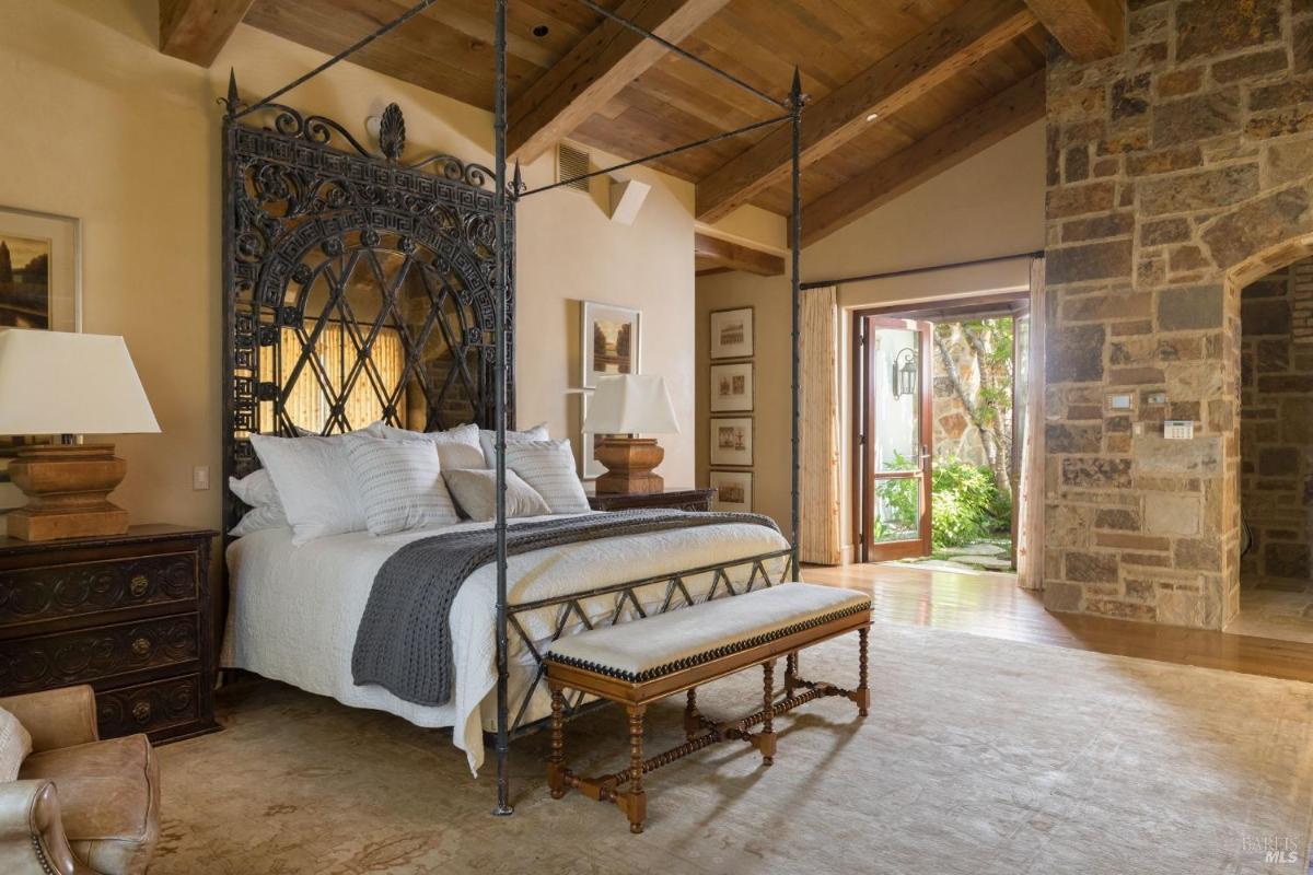 A bedroom featuring a four-poster bed with a metal frame, a wooden bench at the foot of the bed, and two lamps on bedside tables.