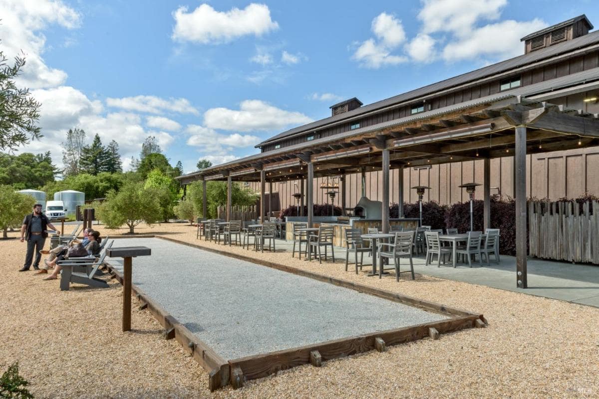 Outdoor seating area with tables, chairs, and a bocce court next to a building.