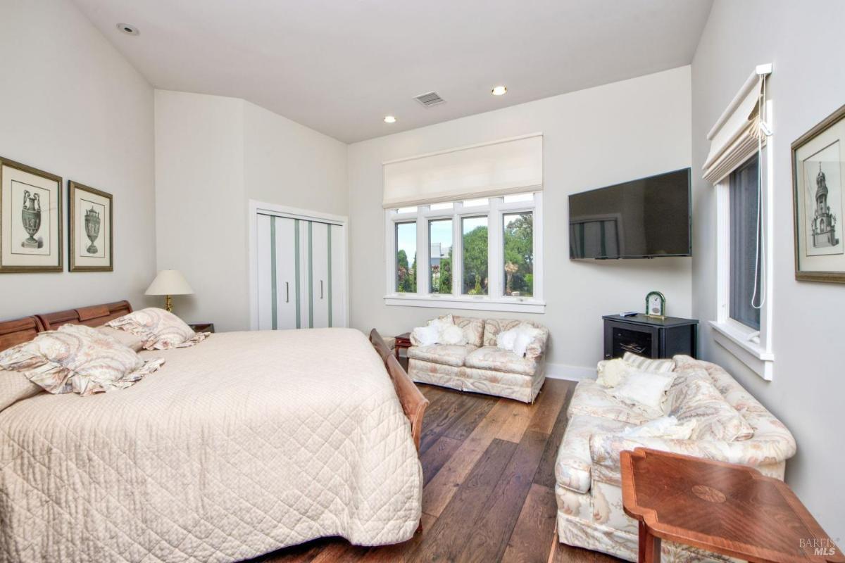 A bedroom with a large bed, closet, seating area, and a wall-mounted TV.