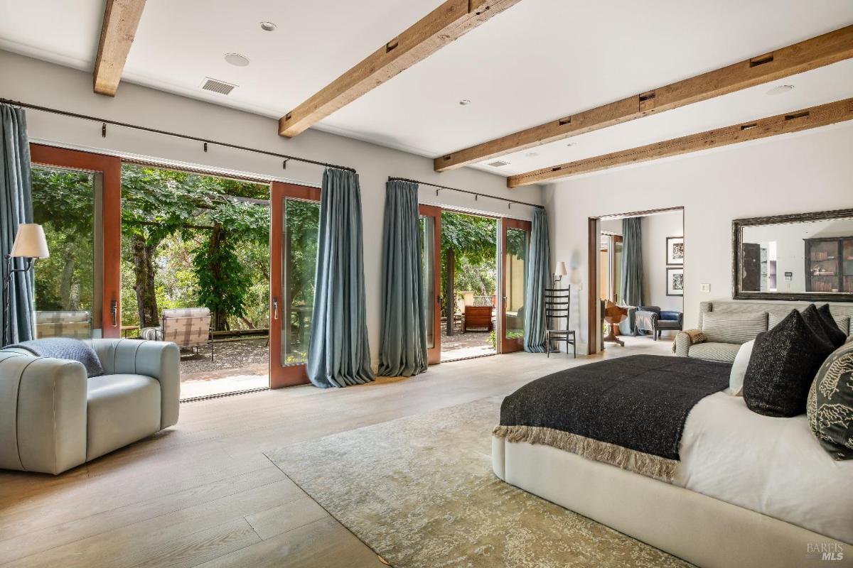 Bedroom with large windows and curtains, opening to an outdoor patio.