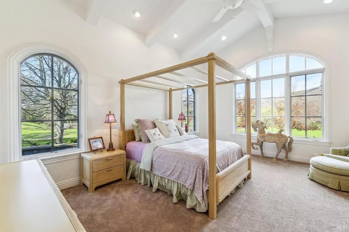 Bedroom with a four-poster bed, vaulted ceilings, and arched windows overlooking the outdoor greenery.