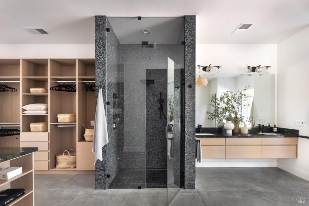 A bathroom with a glass-enclosed shower, dual vanity, and a built-in closet with open shelving and hanging space.