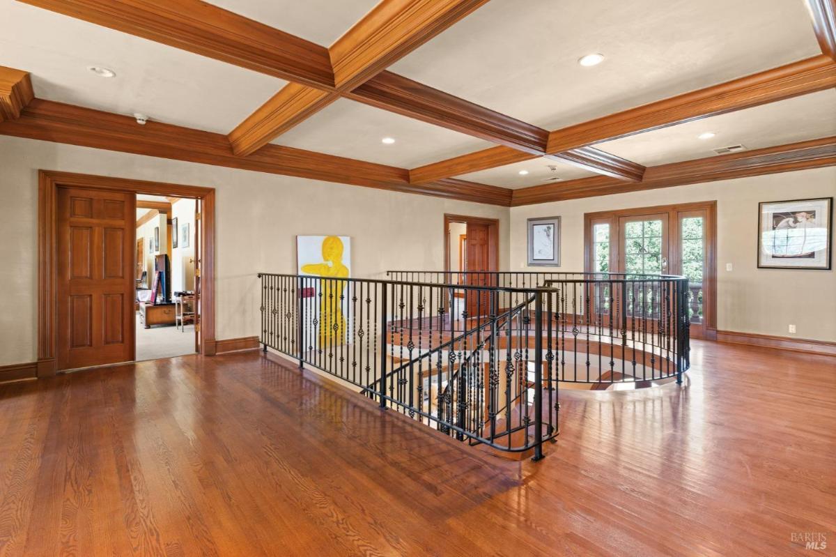 Second-floor hallway with wood detailing, iron railing, and access to bedrooms.