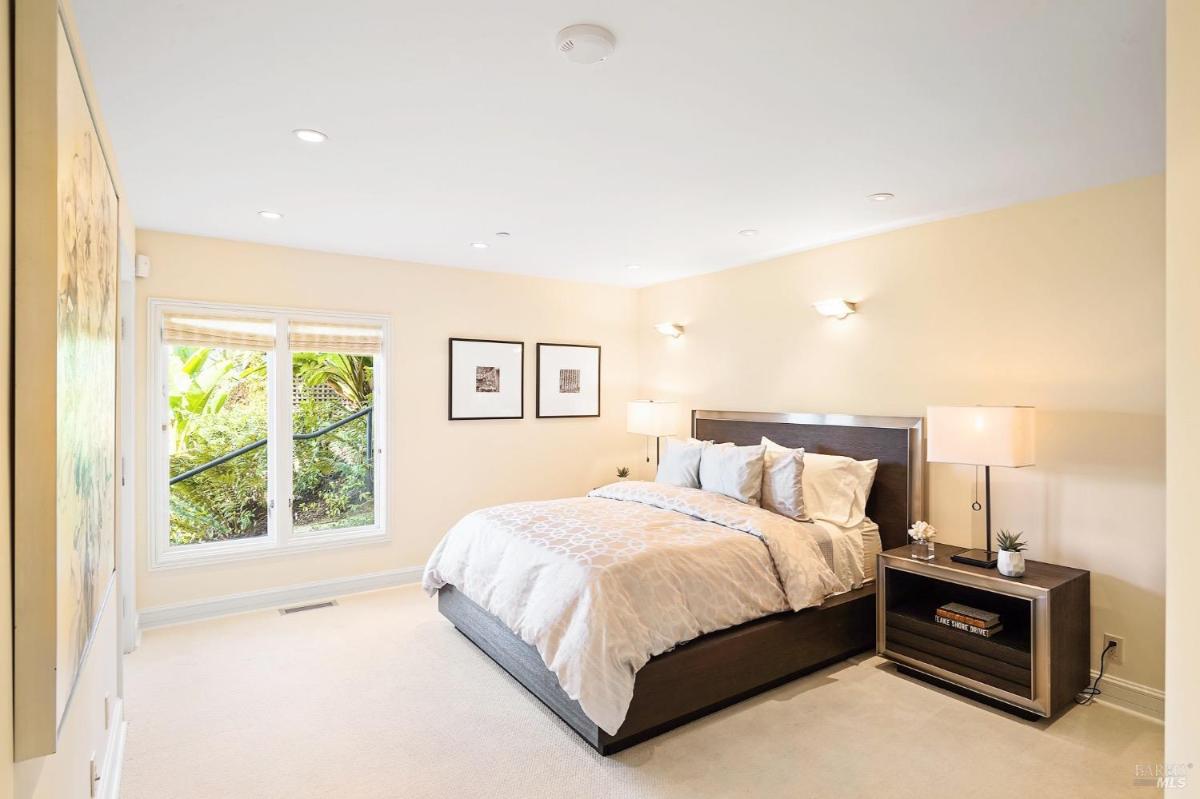 Bedroom with a large window overlooking greenery, a dark wood bed frame, and matching nightstands.