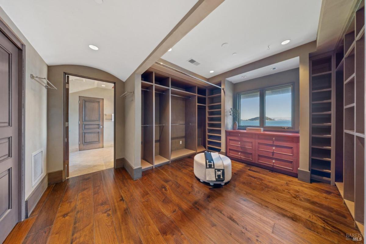 A walk-in closet featuring wooden flooring, built-in shelves, and large windows that provide natural light. 