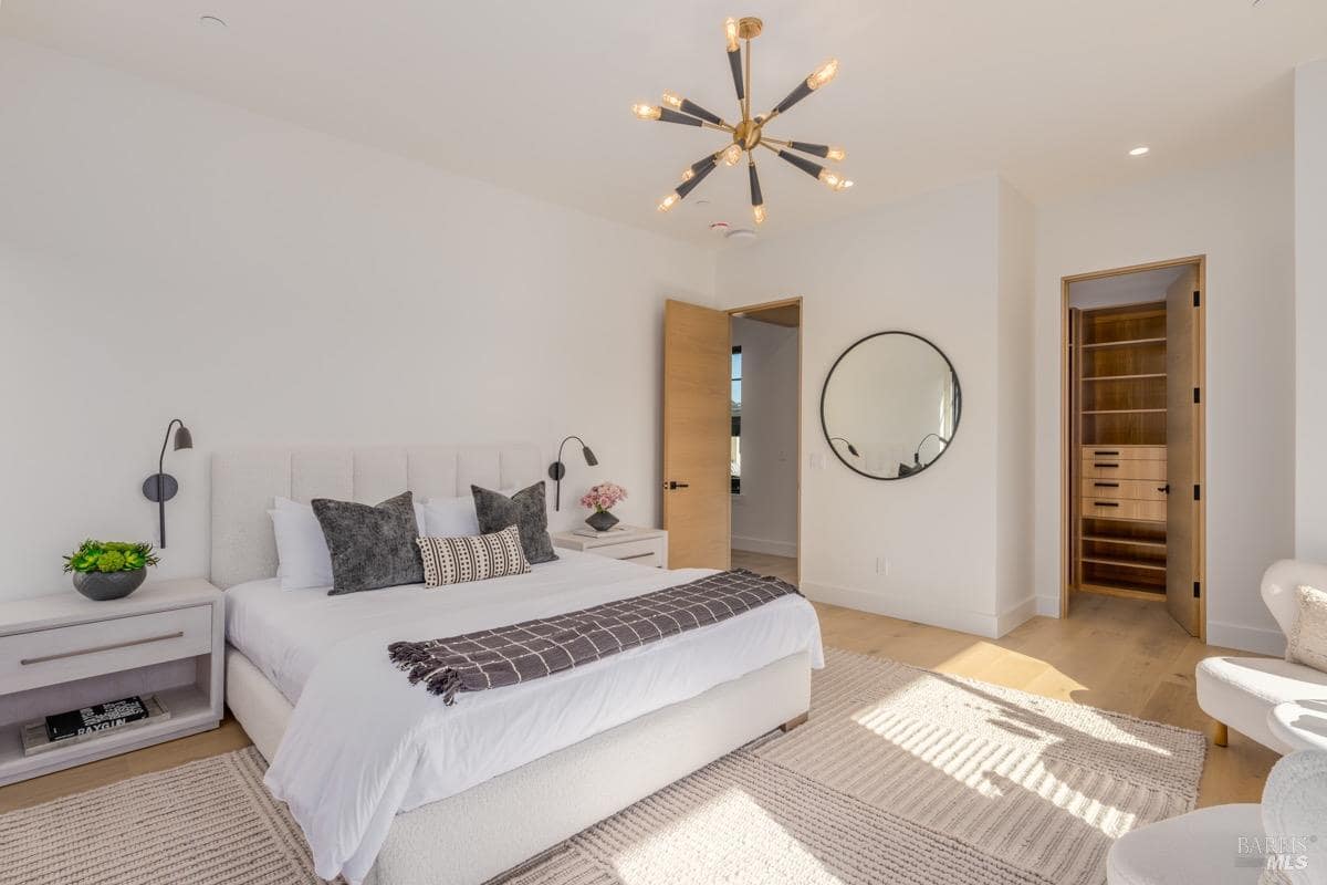 A bedroom with a modern chandelier, upholstered bed, nightstands, and an open walk-in closet.