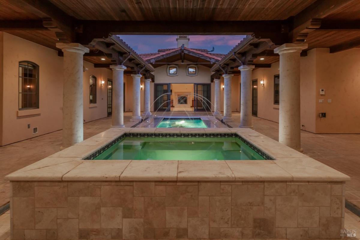 A swimming pool is flanked by columns and arches with a water feature.