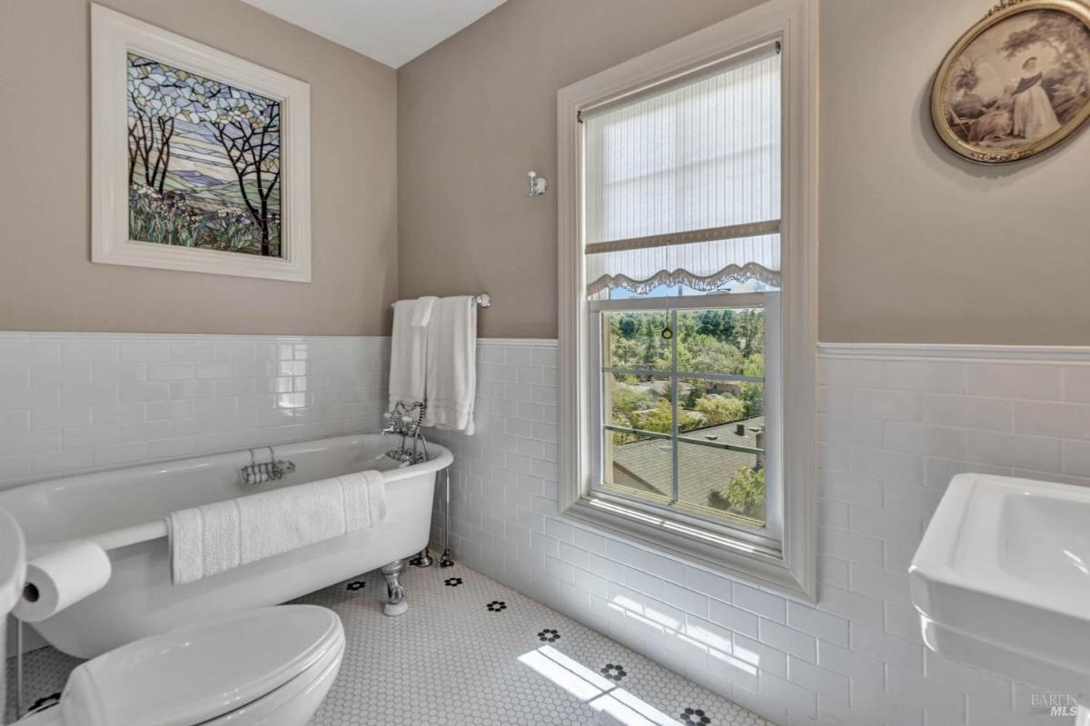 A bathroom with a freestanding clawfoot tub, tile walls, and a large window.