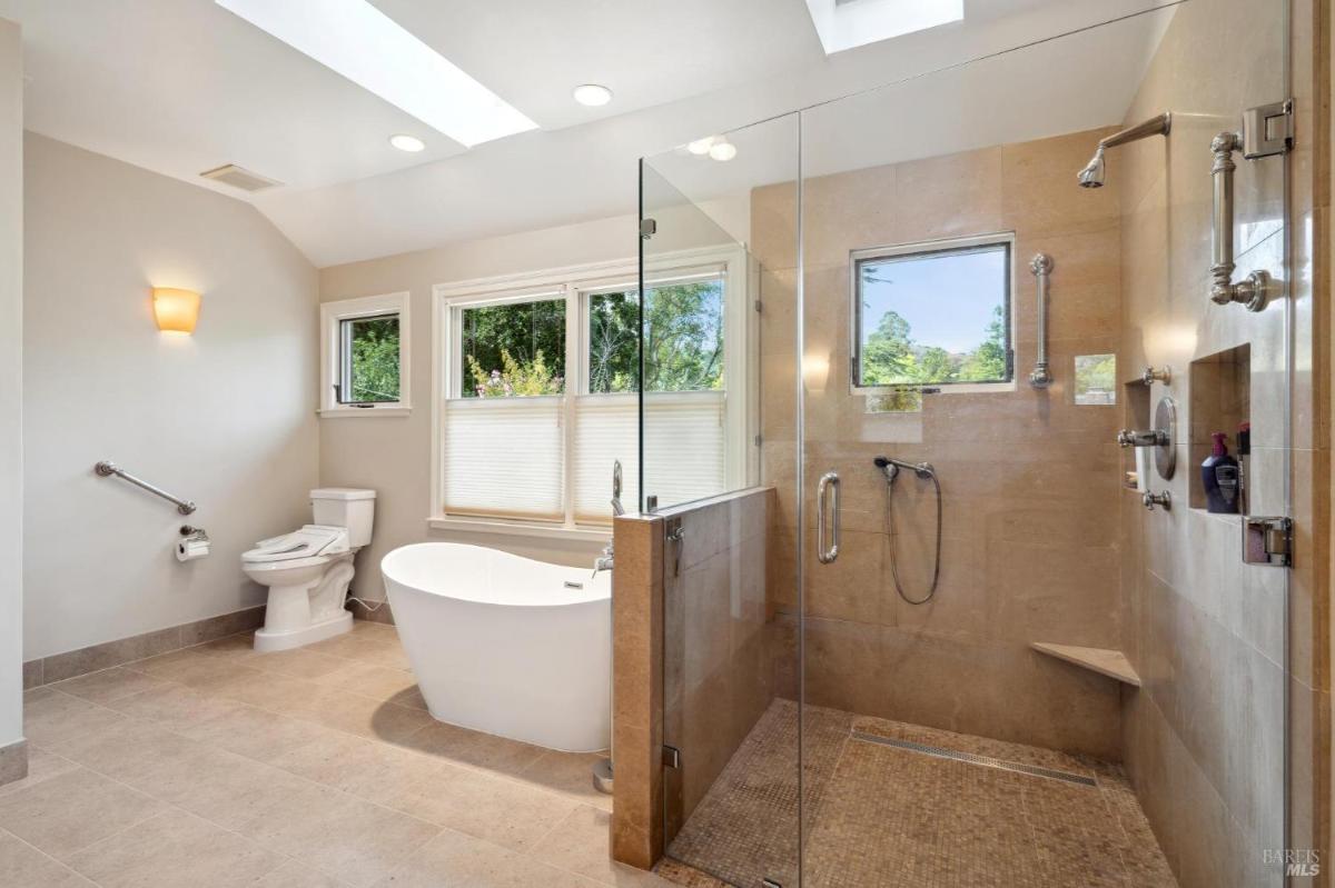 Bathroom with a freestanding tub, glass shower enclosure, and windows.