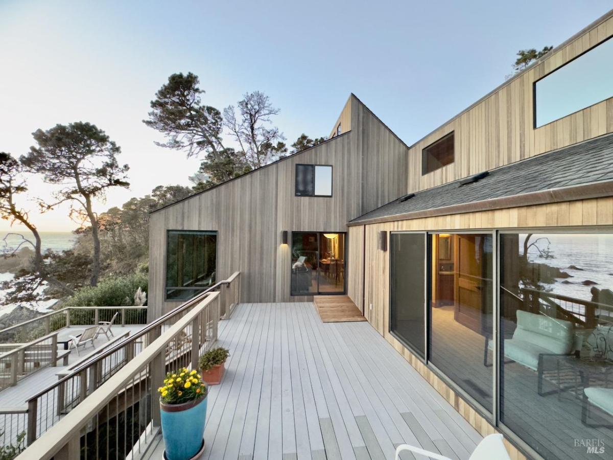 A house exterior with wooden siding, large windows, and a wraparound deck.