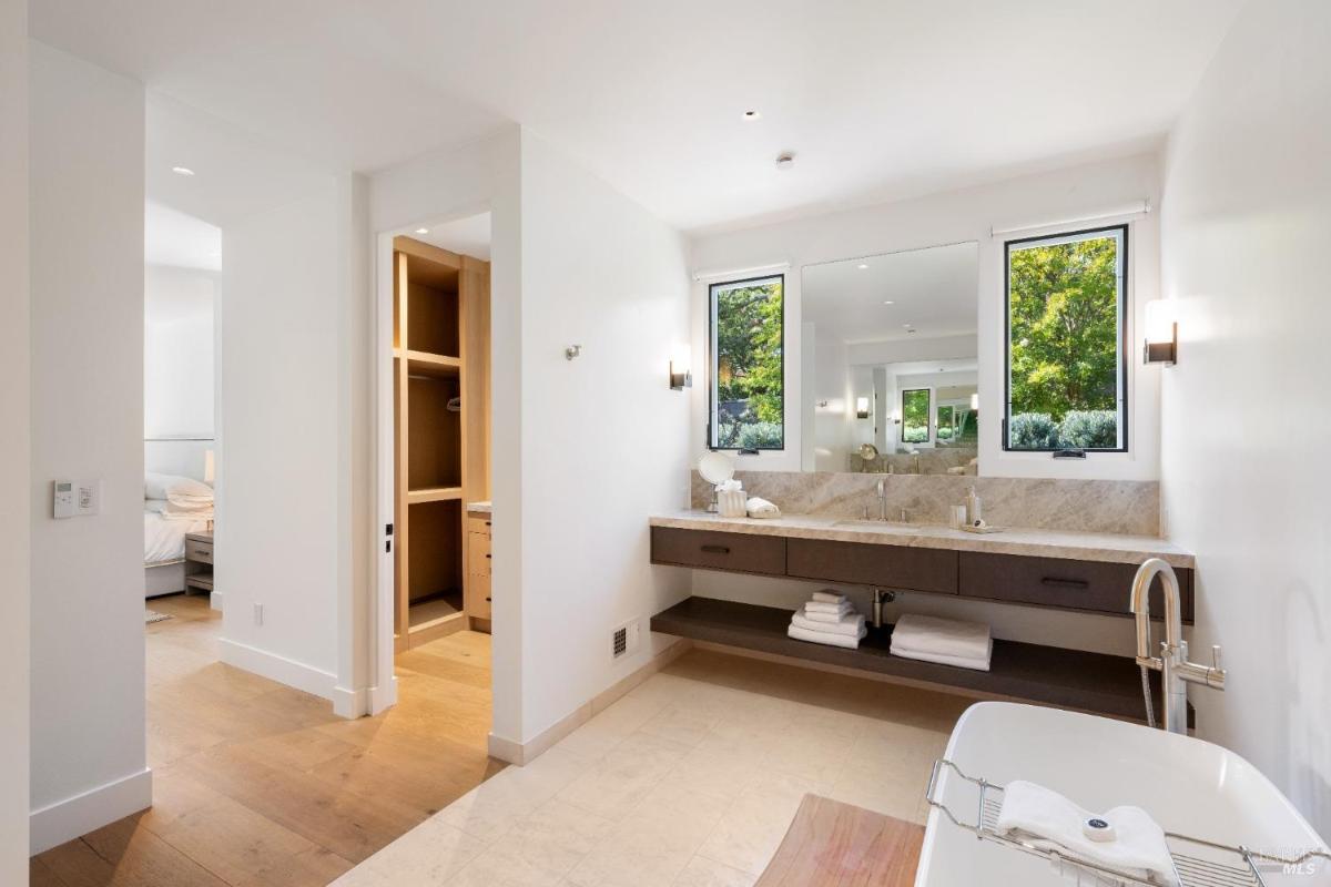 A bathroom with a double sink vanity, a soaking tub, and windows overlooking greenery.