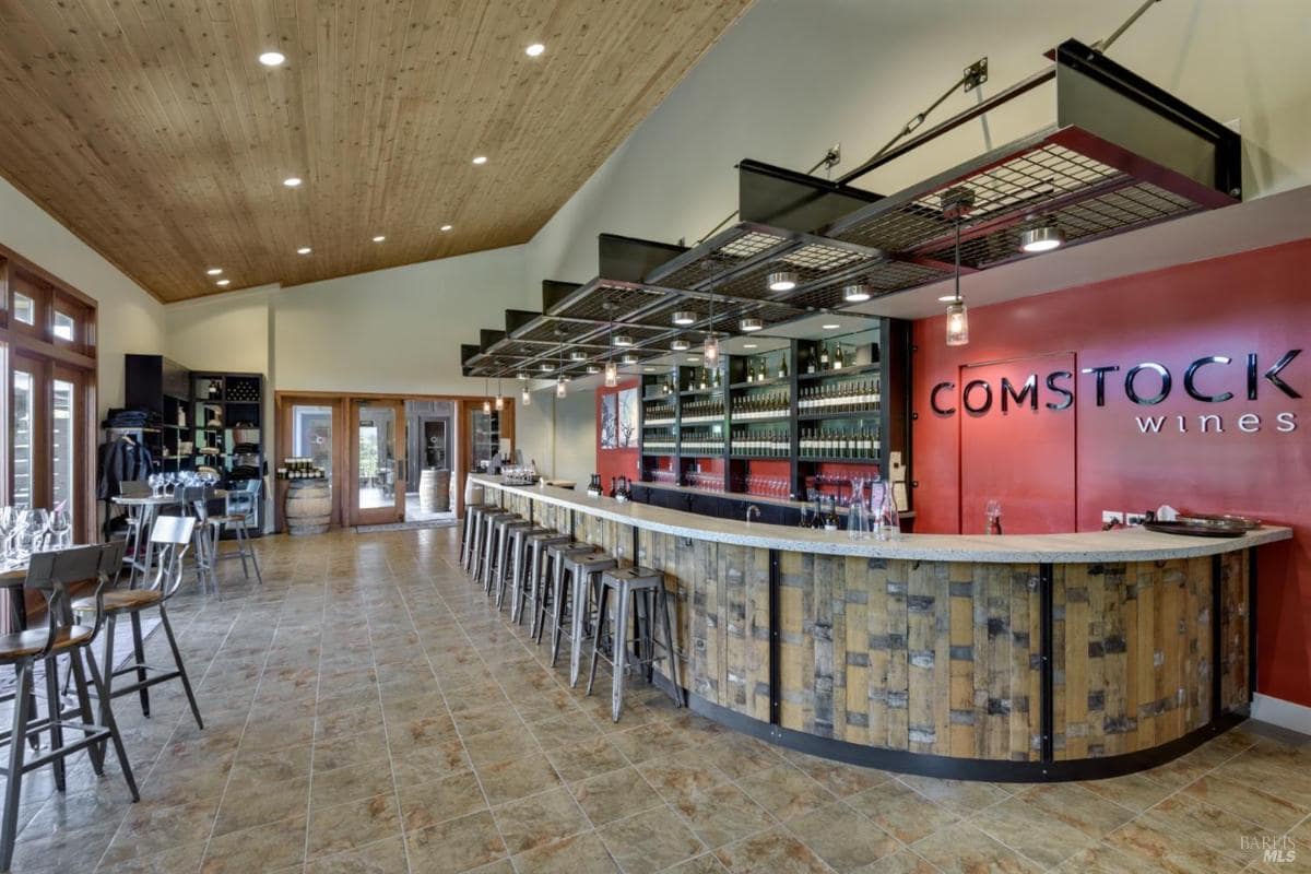 Wine tasting room with a long bar, shelves of bottles, and seating areas.