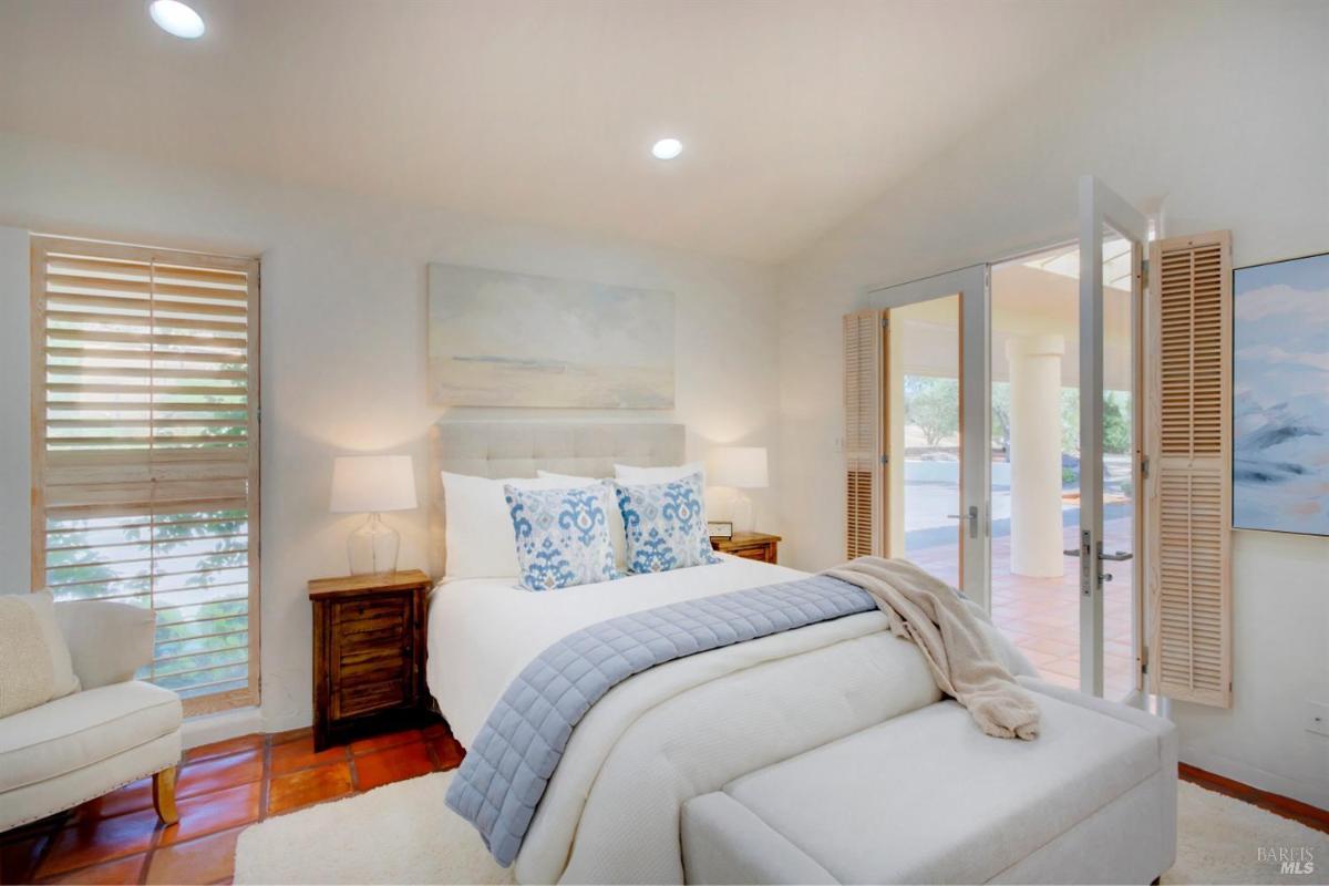 A bedroom with a bed, armchair, and doors opening to a covered outdoor space.