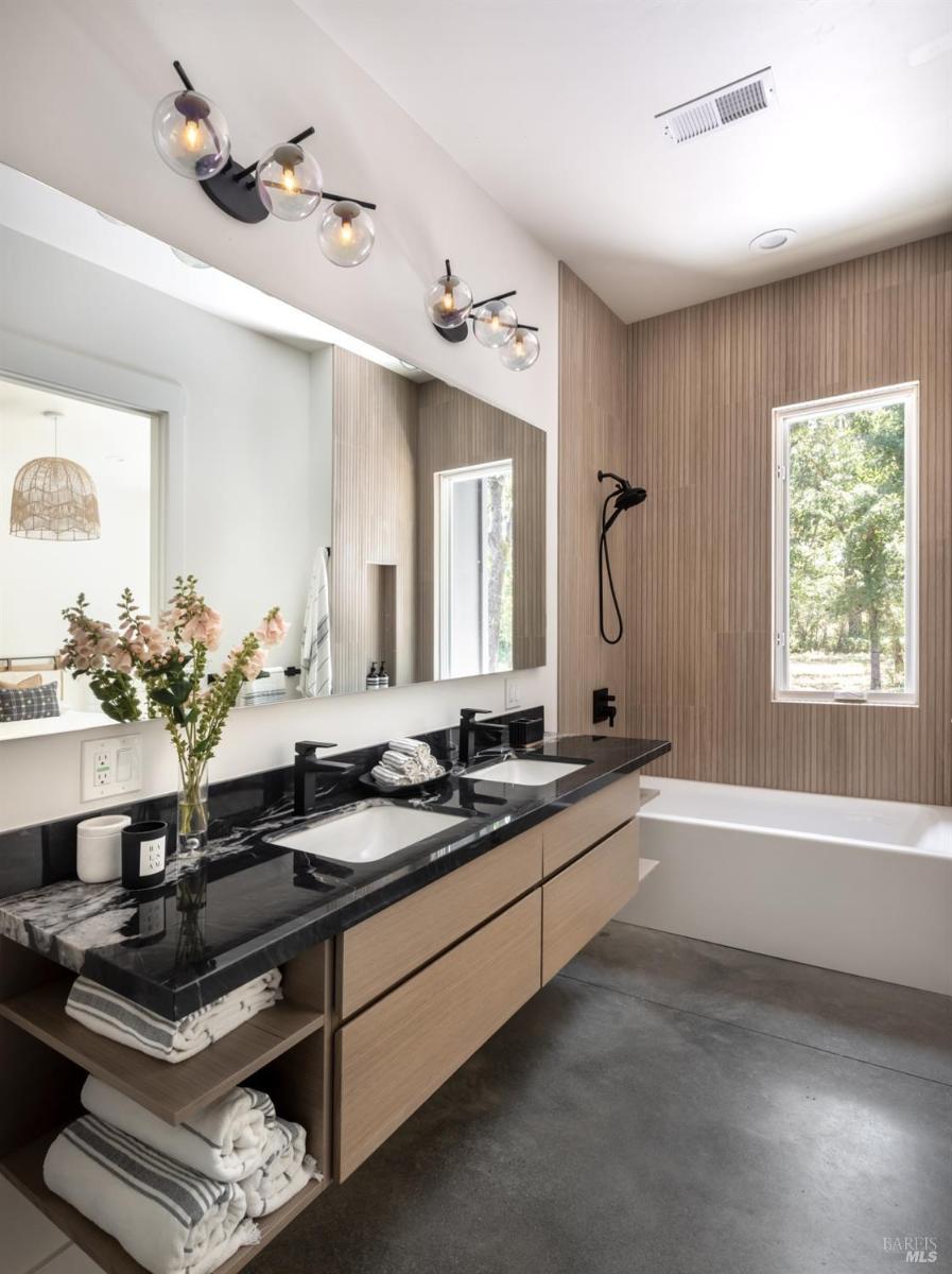 A bathroom featuring a double vanity with black countertops, a built-in bathtub, and vertical wood paneling on the wall.