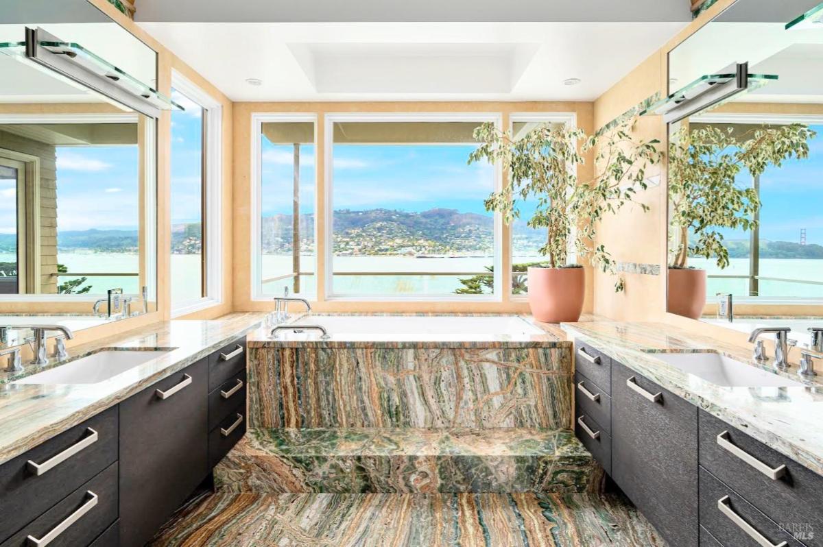 A luxurious bathroom showcasing a marble tub, dual vanities, and expansive windows with panoramic water views.