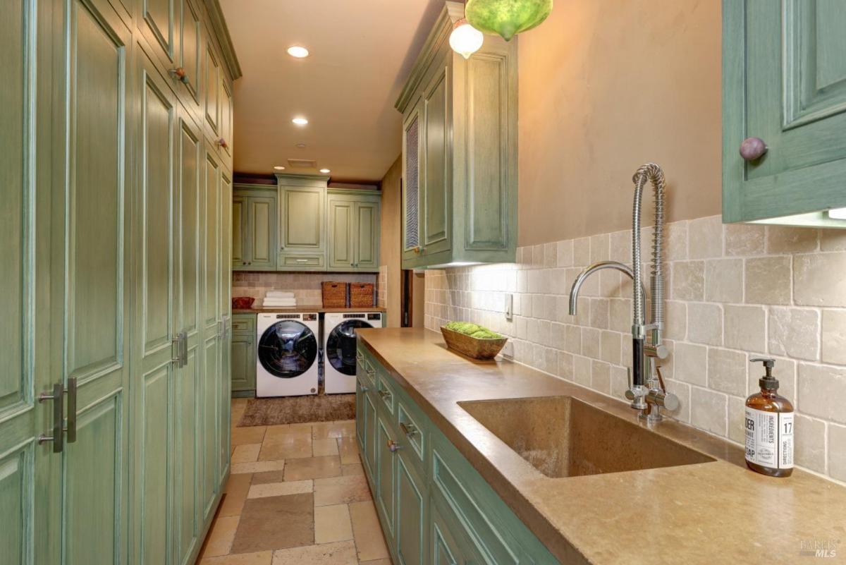 Laundry room with green cabinetry, a stone countertop, and modern appliances. 