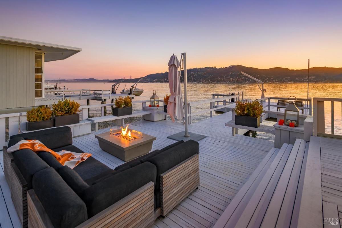 Waterfront deck with firepit and marina view at sunset.