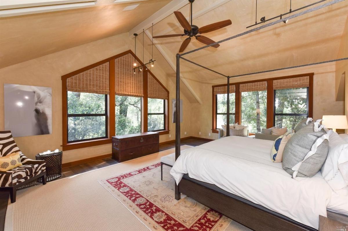 A bedroom with a canopy bed, large windows, and a seating area.