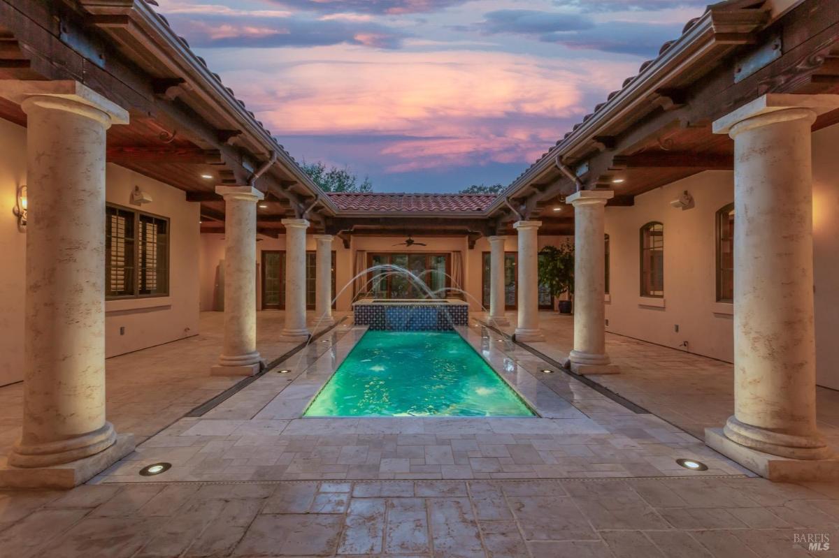 A swimming pool is flanked by columns and arches with a water feature.