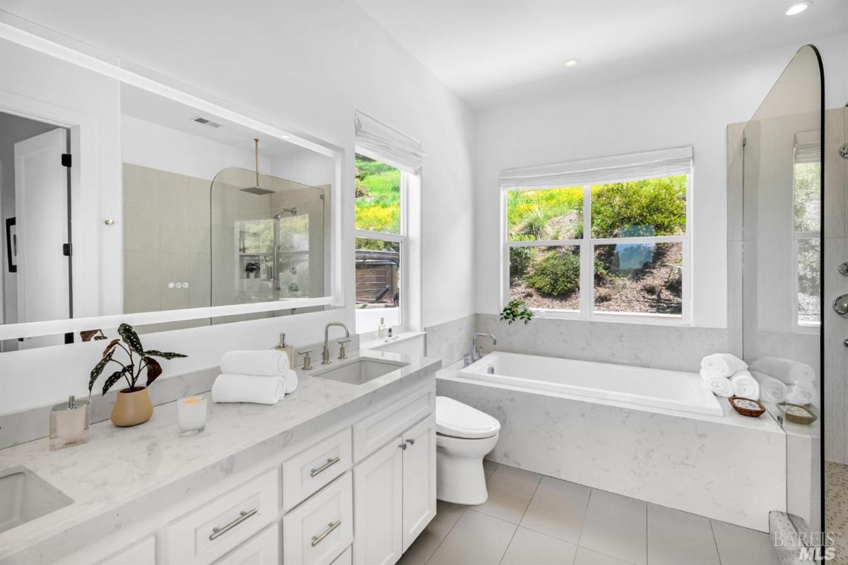 A modern bathroom with a sleek design featuring a double sink vanity, a large mirror, and a bathtub. 