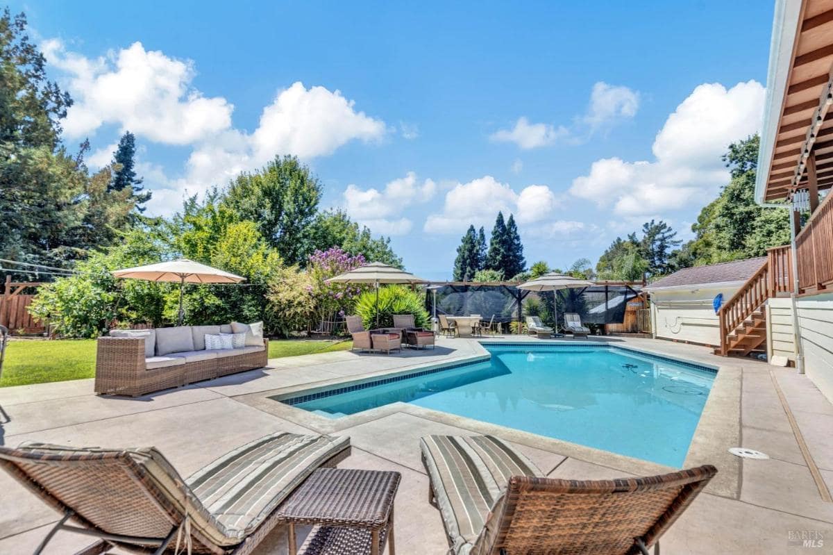 A backyard pool area with lounge chairs, patio furniture, and umbrellas.