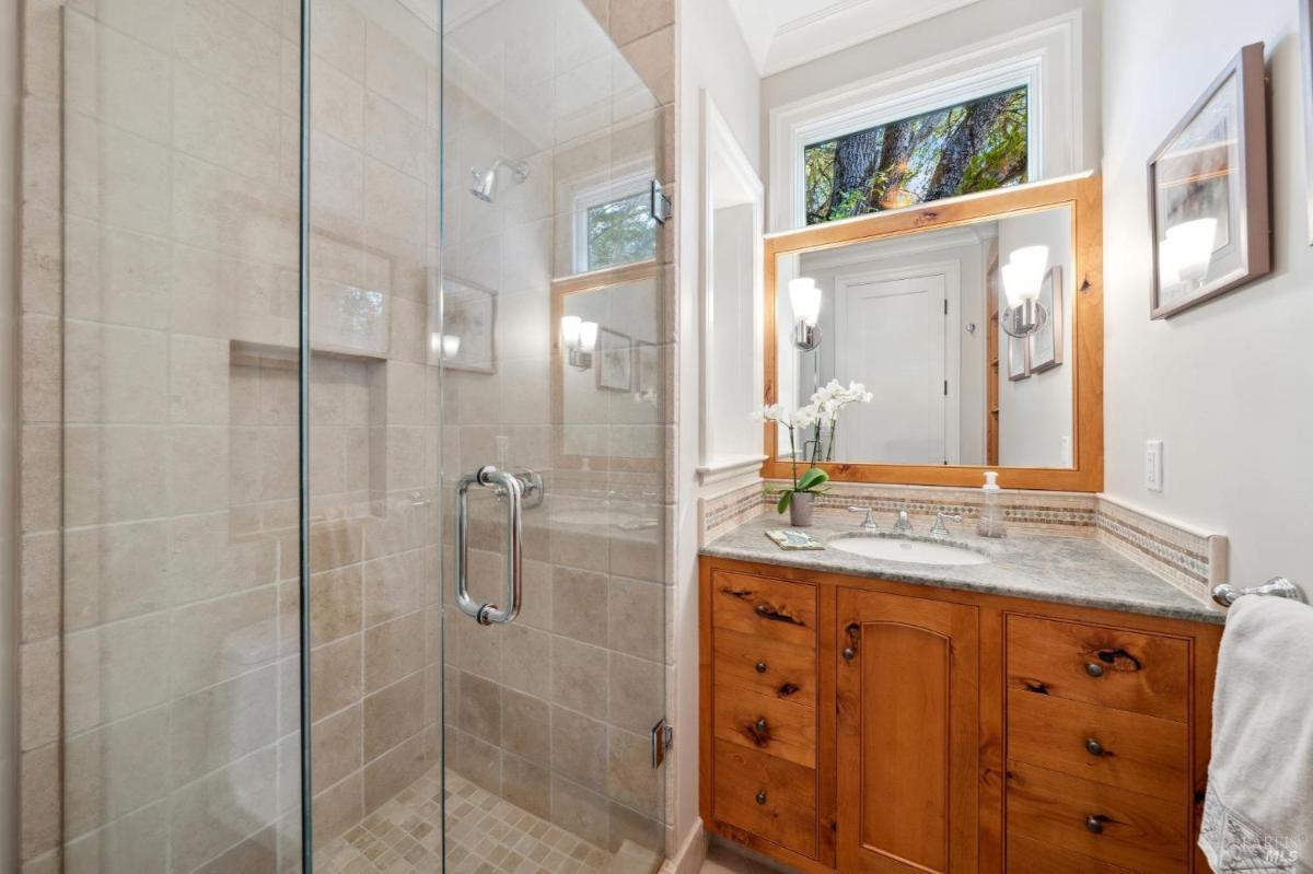 Bathroom vanity with a single sink, wooden cabinets, and a glass shower.