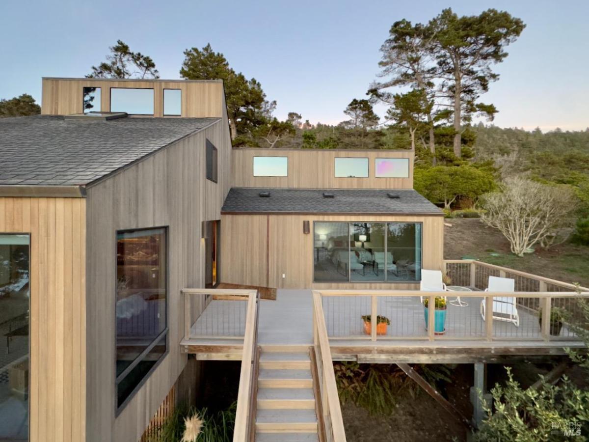 A rear view of the house with a staircase leading to the deck and large glass doors.