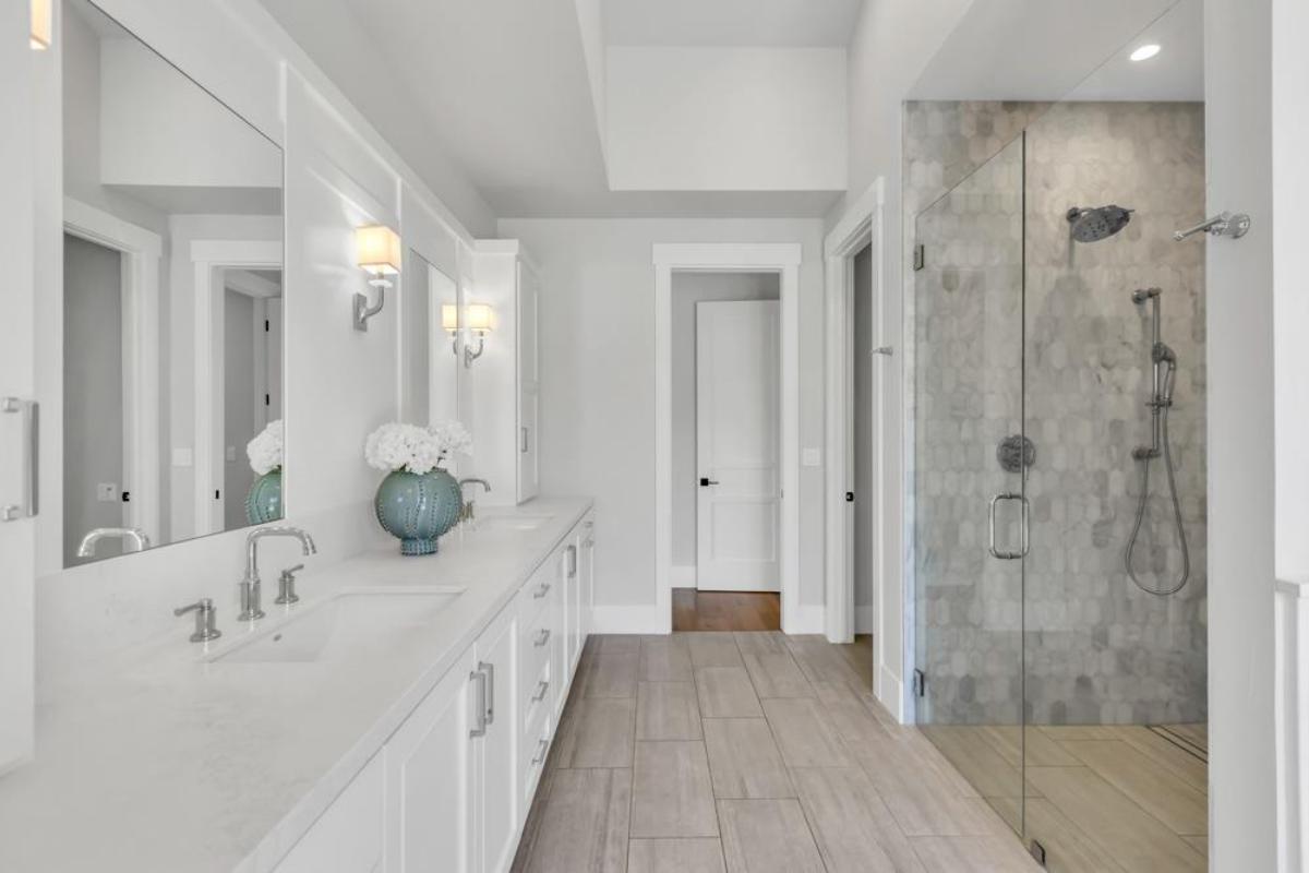 A bathroom with a double vanity, mirrors, and a glass shower enclosure.